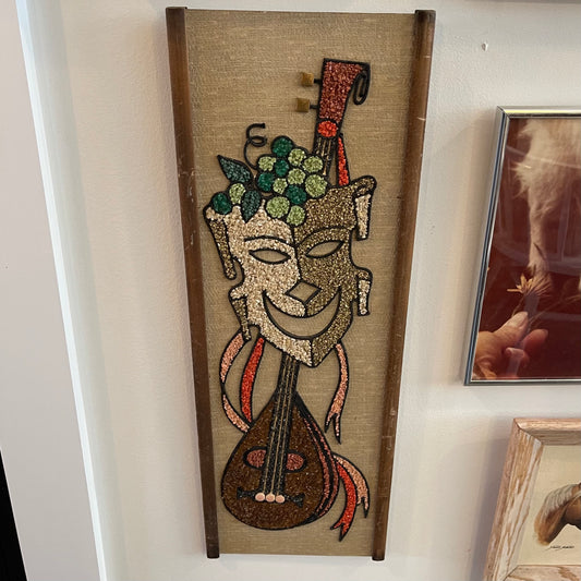 Decorative wall art with a stylized face and musical instrument on a textured background