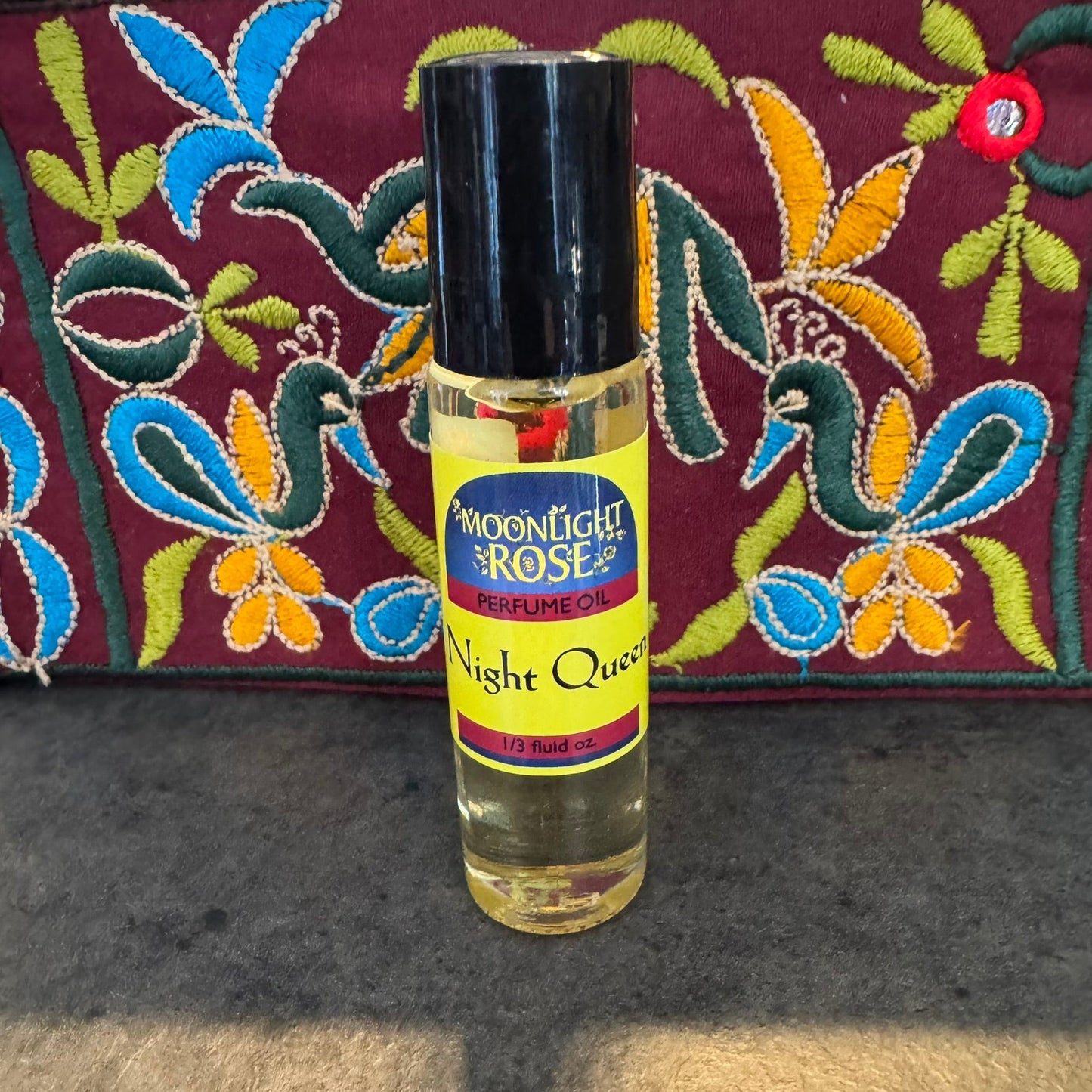 Perfume oil bottle labeled 'Moonlight Rose' with a colorful embroidered background