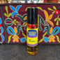 Perfume oil bottle labeled 'Moonlight Rose Rasta' on a textured surface with a colorful embroidered background.