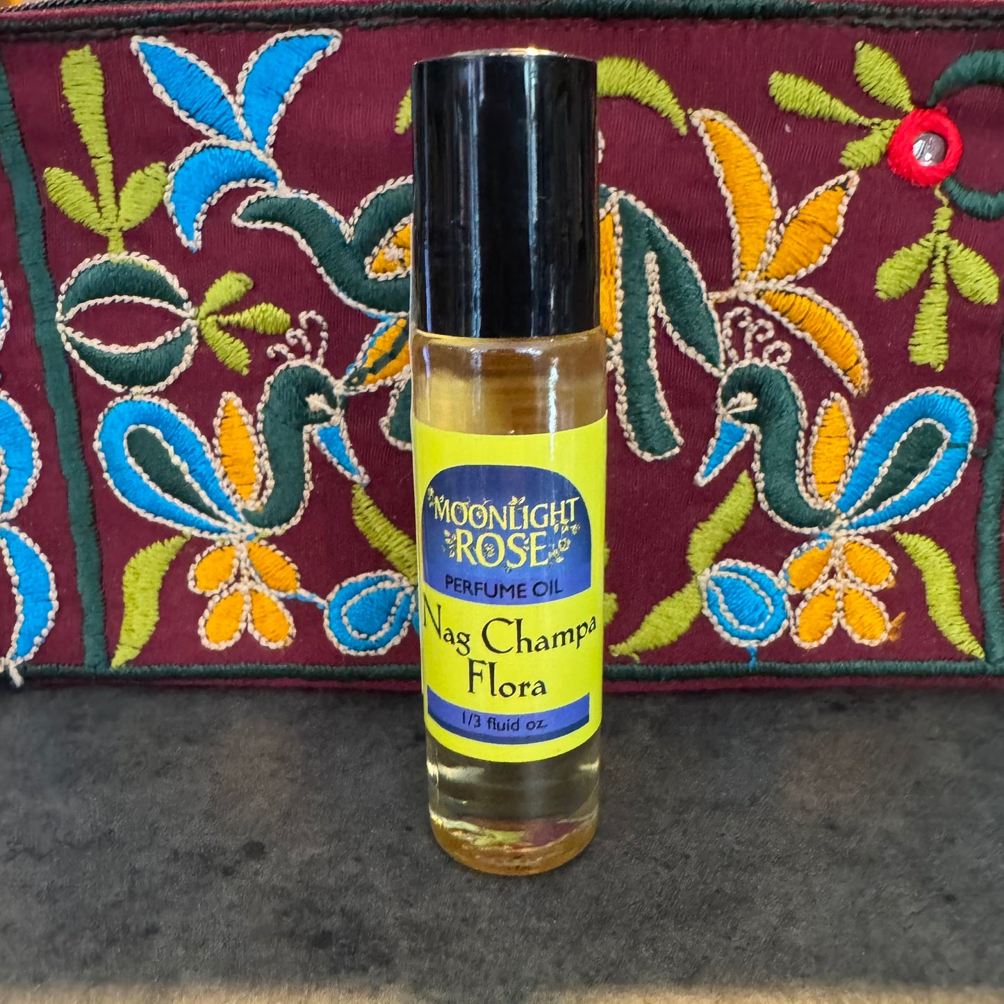 Perfume oil bottle labeled 'Nag Champa Flora' with a colorful embroidered background