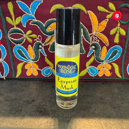 Perfume oil bottle labeled 'Egyptian Musk' by Moonlight Rose on a textured surface with a colorful embroidered fabric background.