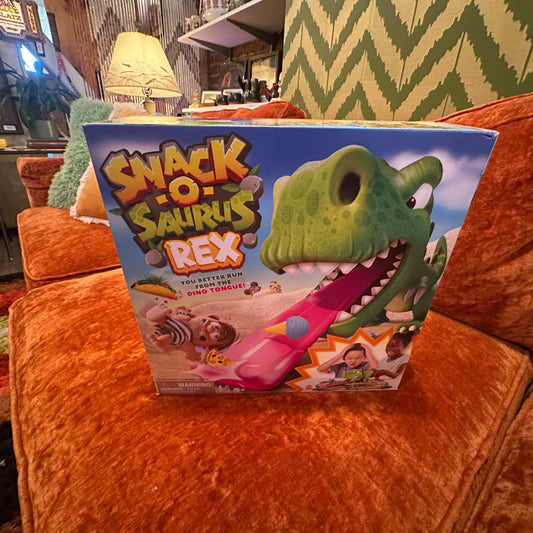 Snack-O-Saurus Rex toy packaging on an orange couch with a room in the background